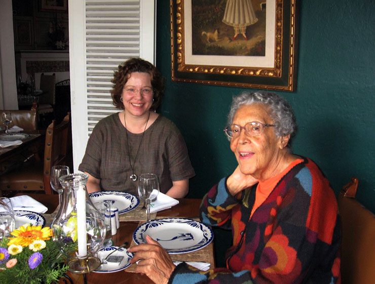 Elizabeth Catlett and another woman sit at a dining table and smile at the camera