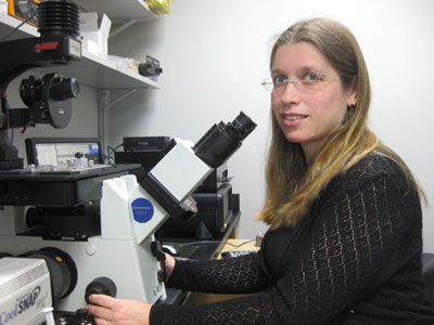 Sarit Smolikove sits at a microscope and looks into the camera