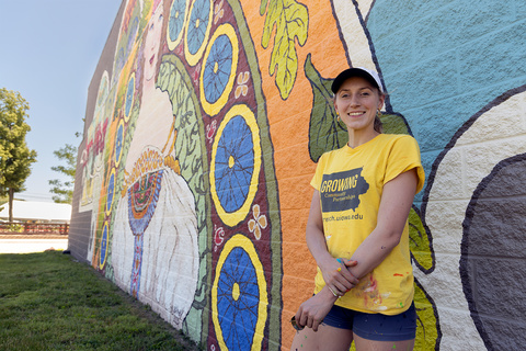 Artist Ali Hval stands next to her mural in Czech Village, Cedar Rapids.