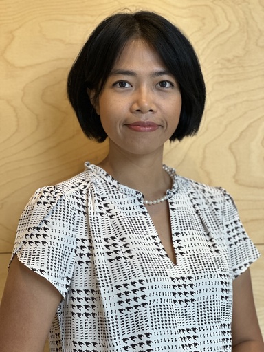 Dr. Aung poses for a photo wearing a white short-sleeve blouse with a black checkered pattern on it.