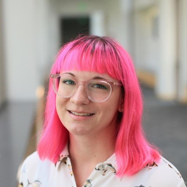Dr. Katelyn Joyal poses for a photo wearing a white collared shirt. Her hair is bright pink.