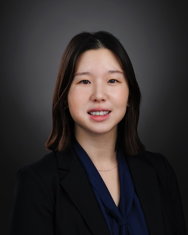 Jean Hong smiles as the camera wearing a black V-neck top. Her hair is down behind her shoulders.