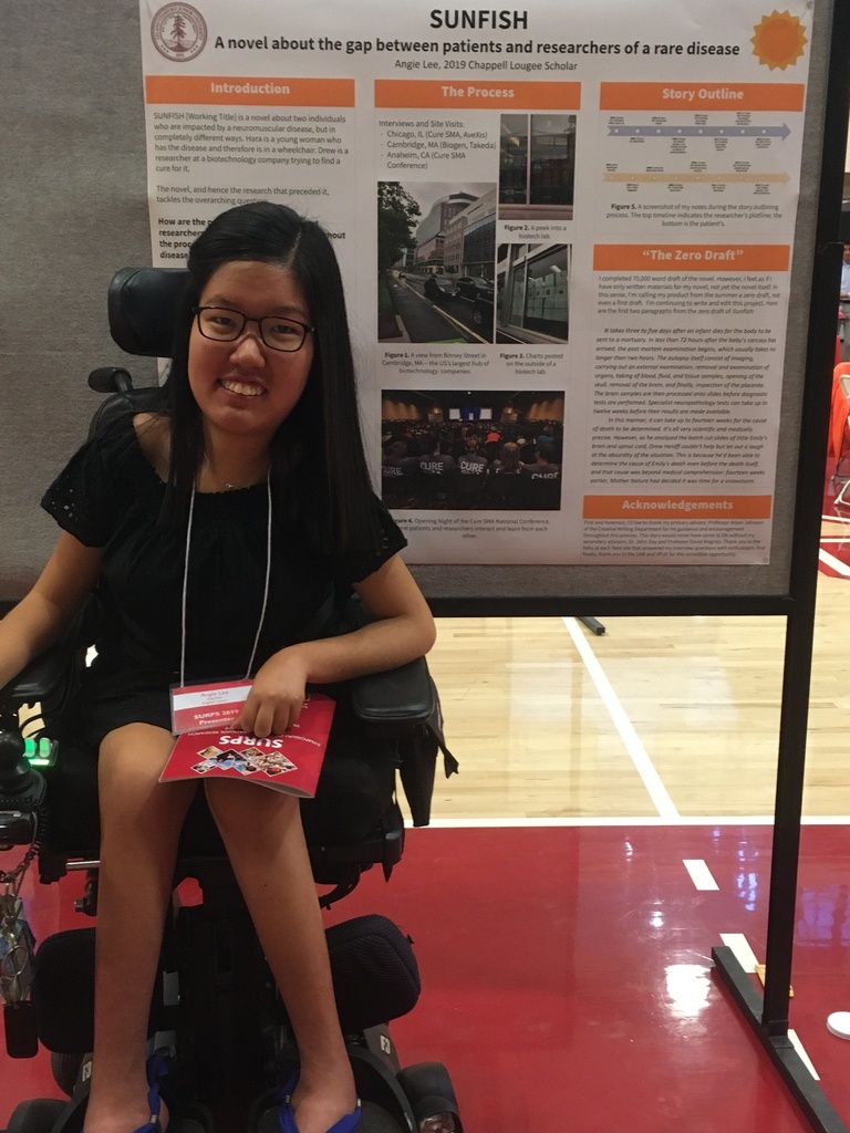 Angie Lee seated in her wheelchair in front of a poster presentation of her research