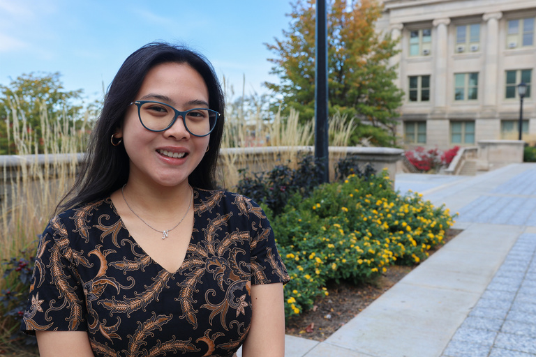 Fascha sits on a bench on the west side of the Pentacrest. She wear a black and gold top and glasses.