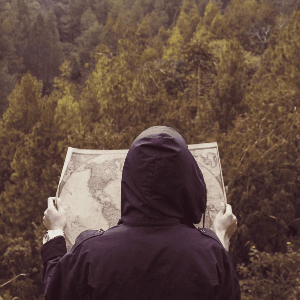 hooded figure examining map while overlooking forest