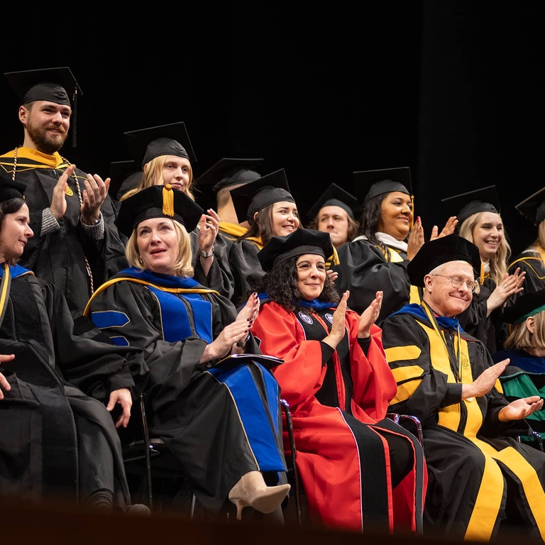 Fall commencement 2024 faculty applauding masters graduates on stage